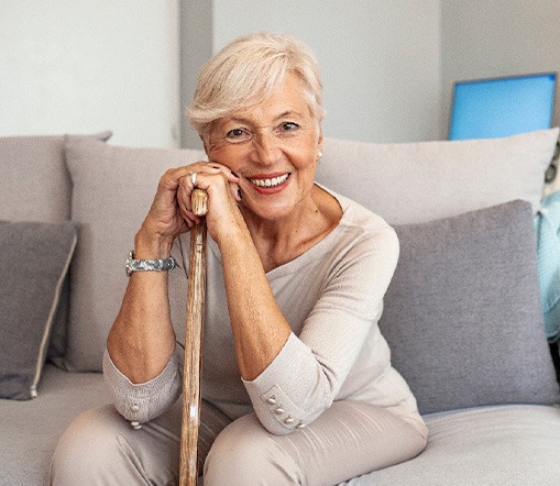 Woman in beige clothes on beige couch leaning on cane smiling