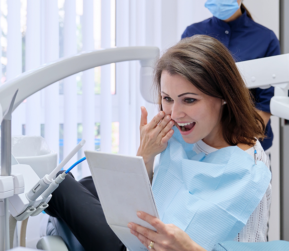 Woman sitting in dental chair checking smile in handheld mirror